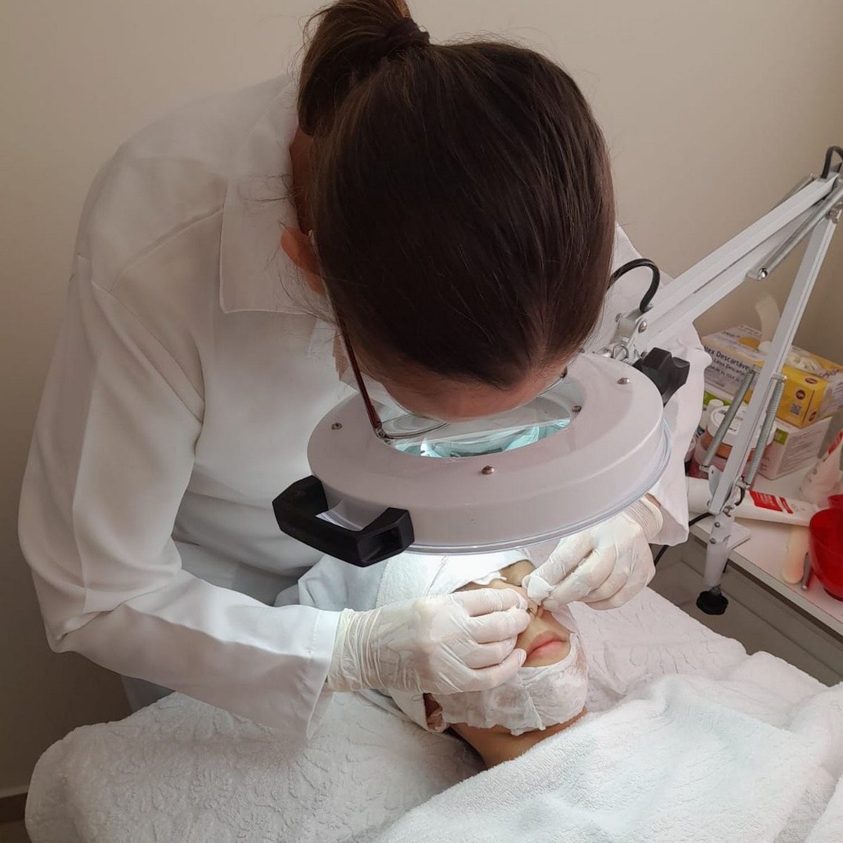Profissional de jaleco e luvas atendendo sob a lupa acesa no salão Omux
